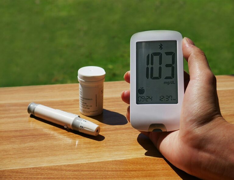 a person holding a blood glucose meter next to a bottle of test strips